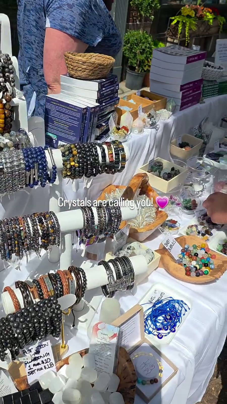 Bracelet bars in front of stacked crystal books, with bowls of loose beads and small tumbles across the table behind them.